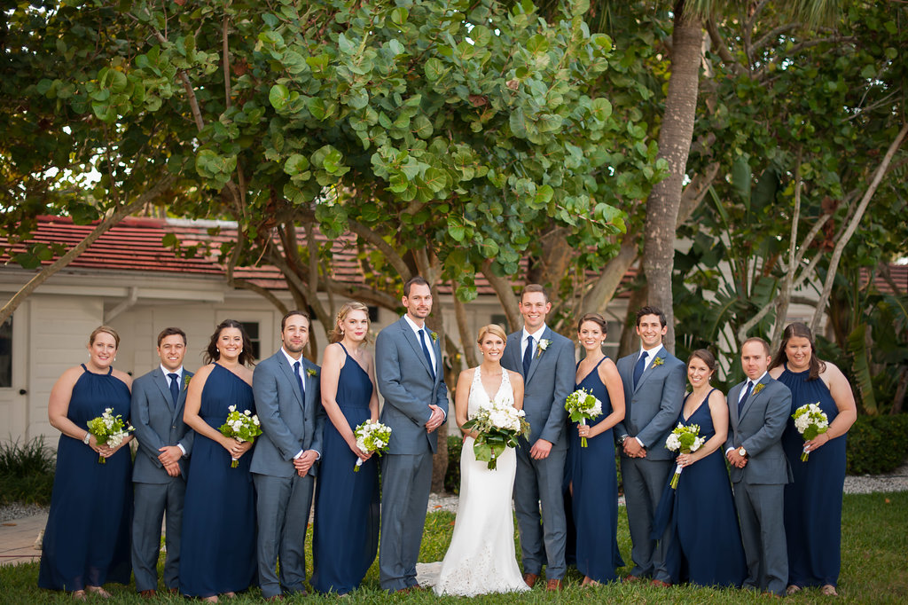 Outdoor Wedding Party Portrait in Navy Blue Mismatched Joanna August Dresses, Bride in BHLDN by Watters Tulle and Lace Applique Sweetheart Plunging Neckline with Lace Straps and Greenery and White Floral Bouquets, Groomsmen in Blue Suits with Blue Ties | Tampa Dress Shop Bella Bridesmaids