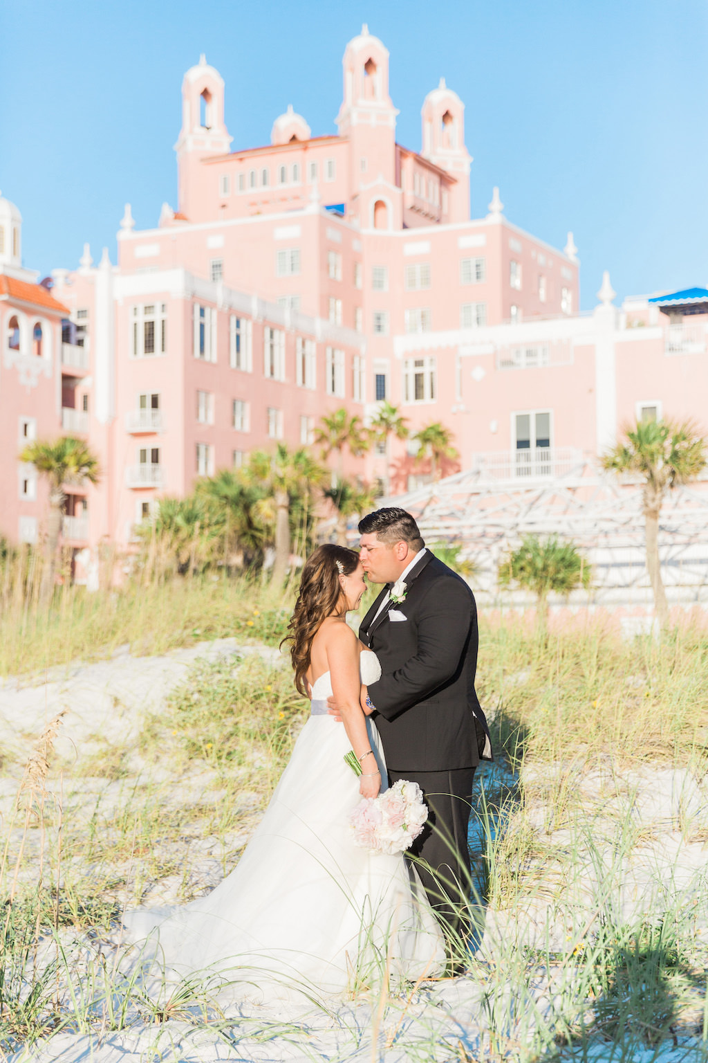 Outdoor Beach Bride and Groom Wedding Portrait in Ballgown Wedding Dress and Grey Sash with White and Pink Rose Bouquet, Groom in Black Tuxedo with White Floral Boutonniere | Historic St Pete Waterfront Hotel Wedding Venue The Don CeSar
