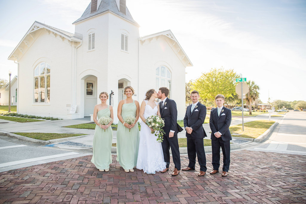 Outdoor Bride, Groom, Bridesmaids and Groomsmen Portrait, Bridesmaids in Sagr Green Matching Dresses with Baby's Breath Bouquets, Groom and Groomsmen in Navy Blue Suits, Sage Green Ties and Brown Wing Tipped Dress Shoes | Tampa Bay Photographer Kristen Marie Photography | Venue Tampa Bay Photographer Kristen Marie Photography | Venue Outdoor Wedding Portrait, Bride in A-Line Lace and Cap Sleeve Wedding Dress and Veil, Greenery and White Floral Bouquet | Tampa Bay Photographer Kristen Marie Photography | Outdoor Bride and Groom Wedding Portrait, Bride in A-Line Lace and Cap Sleeve Wedding Dress and Veil | Tampa Bay Photographer Kristen Marie Photography | Venue Palm Harbor White Chapel and Harbor Hall