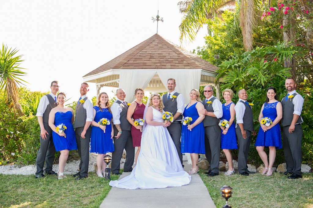 Outdoor Bride, Groom, Bridesmaids, and Groomsmen Wedding Portrait, Bridesmaids in Short Royal Blue Mismatched Dresses, Groomsmen in Grey Vests and Sunflower Boutonnieres, Maid of Honor in Short Burgundy/Dark Red Dress, with Yellow Sunflower, White, Blue and Greenery Bouquets | Tampa Bay Photographer Andi Diamond Photography | Tampa Venue Rusty Pelican