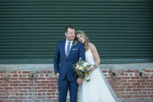 Outdoor Bride Wedding Portrait in A-line Strappy Lace and Tulle Wedding Dress with Greenery, White and Pink Floral Bouquet, Curled Hair Down and Veil, Groom in Navy Blue Suit and Greenery Boutonniere | Tampa Bay Hair and Makeup Femme Akoi Beauty Studio