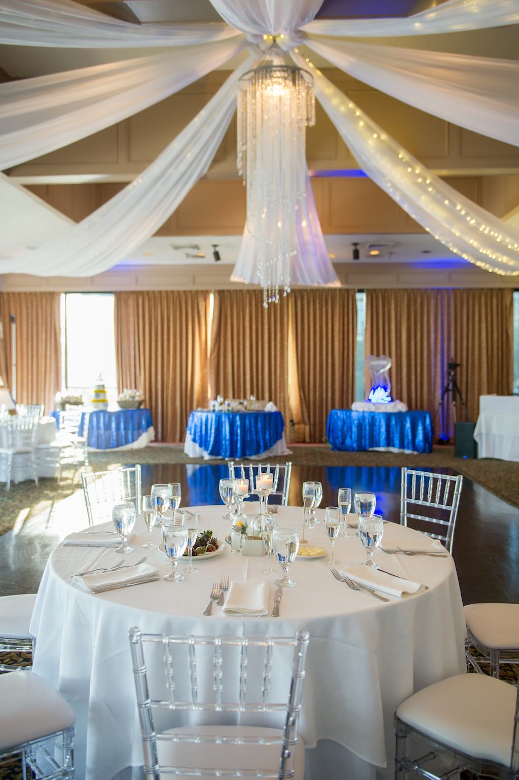 Ballroom Wedding Reception Decor, Round Tables, White and Blue Tablecloths, Clear Acrylic Chiavari Chairs, Crystal Chandelier, Draping and String Lights | Tampa Bay Photographer Andi Diamond Photography | Tampa Venue Rusty Pelican