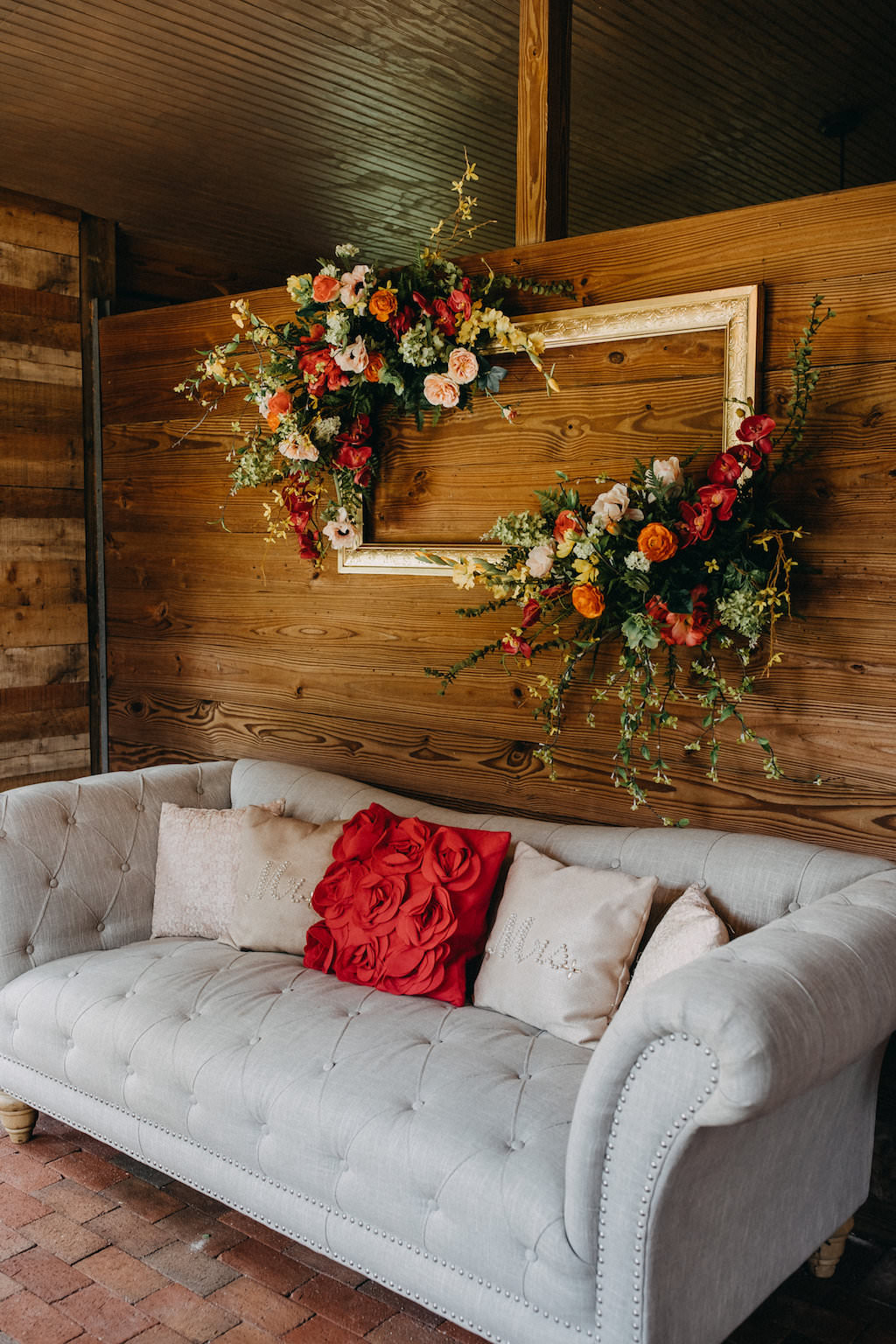 Rustic Tropical Wedding Reception Lounge Seating Decor, Grey Couch with Pillows, Wooden Backdrop, Gold Frame with Tropical Floral Bouquets | Tampa Bay Photographer Rad Red Creative | Rustic Venue Cross Creek Ranch