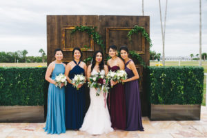 Outdoor Bride and Bridesmaids Wedding Portrait, Bridesmaids in Mismatched Dusty Blue, Navy Blue, Marsala and Plum Dresses with White and Greenery Bouquets, Bride in Sweetheart Strapless Rhinestone Beaded Wedding Dress with White, Pink, Dark Red, and Greenery Bouquet, Wooden Door with Vintage Gold Frames and Greenery Backdrop | Venue Safety Harbor Resort and Spa