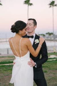 Outdoor Bride and Groom Wedding Portrait, Bride in Strappy Lowback with Ribbon Wedding Dress, Groom in. Black Tuxedo and White Rose Boutonniere | St. Pete Hair and Makeup Femme Akoi