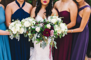 Outdoor Bride and Bridesmaids Wedding Portrait, Bridesmaids in Mismatched Dusty Blue, Navy Blue, Marsala and Plum Dresses with White Roses and Greenery Bouquets, Bride in Sweetheart Strapless Rhinestone Beaded Wedding Dress with White, Pink, Dark Red, and Greenery Bouquet, Wooden Door with Vintage Gold Frames and Greenery Backdrop | Venue Safety Harbor Resort and Spa