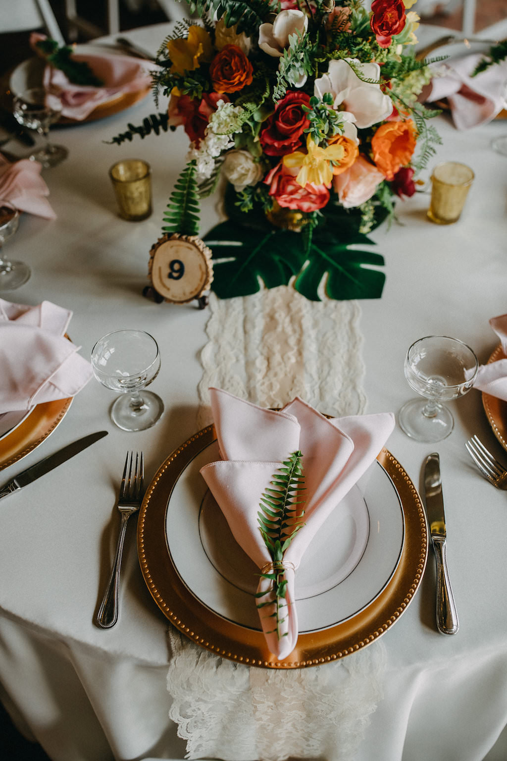Tropical Inspired Wedding Reception Decor, Gold Charger, Blush Pink Linen with Green Leaf, Red, Yellow, Orange, White and Greenery Floral Bouquet on Palm Fronds and Lace Table Runner | Tampa Bay Photographer Rad Red Creative
