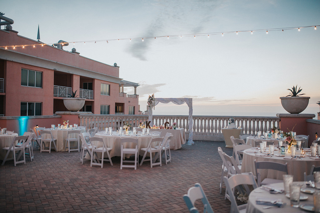 Waterfront Clearwater Beach Hotel Rooftop Wedding Ceremony Decor, Round Tables with White Tablecloths, White Folding Chairs and Arch Wrapped with White Linen and Floral Bouquet | Venue Hyatt Regency Clearwater Beach