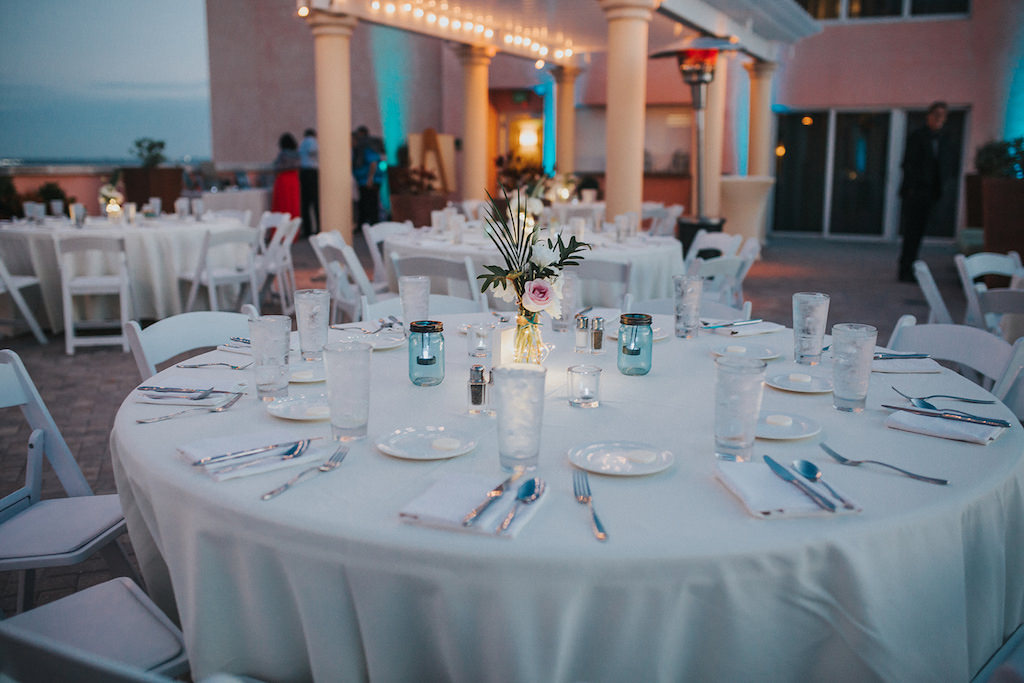 Beachfront Clearwater Beach Hotel Rooftop Wedding Ceremony Decor, Round Tables with White Tablecloths, White Folding Chairs, Blush Pink and Greenery Florals in Vase and Blue Mason Jars | Venue Hyatt Regency Clearwater Beach