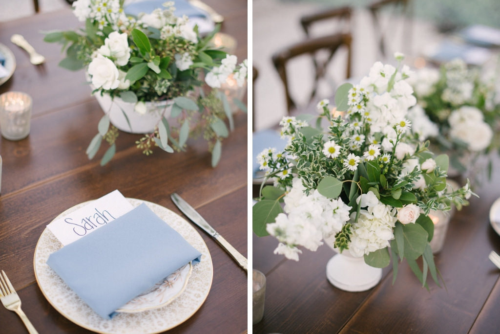Long Wooden Feasting Table with Wood Crossback Chairs, Low White Vases with White and Greenery Floral Centerpieces, Silver Candle Votives, and Pale Blue Napkin Linen on Antique China Plates | Tampa Bay Rental Company A Chair Affair