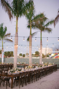 Outdoor Lounge Area with String Lights, Long Wooden Feasting Tables, Wood Crossback Chairs, Low White Vase with White and Greenery Floral Centerpieces at Unique Wedding Venue St Petersburg Intermezzo Coffee and Cocktails