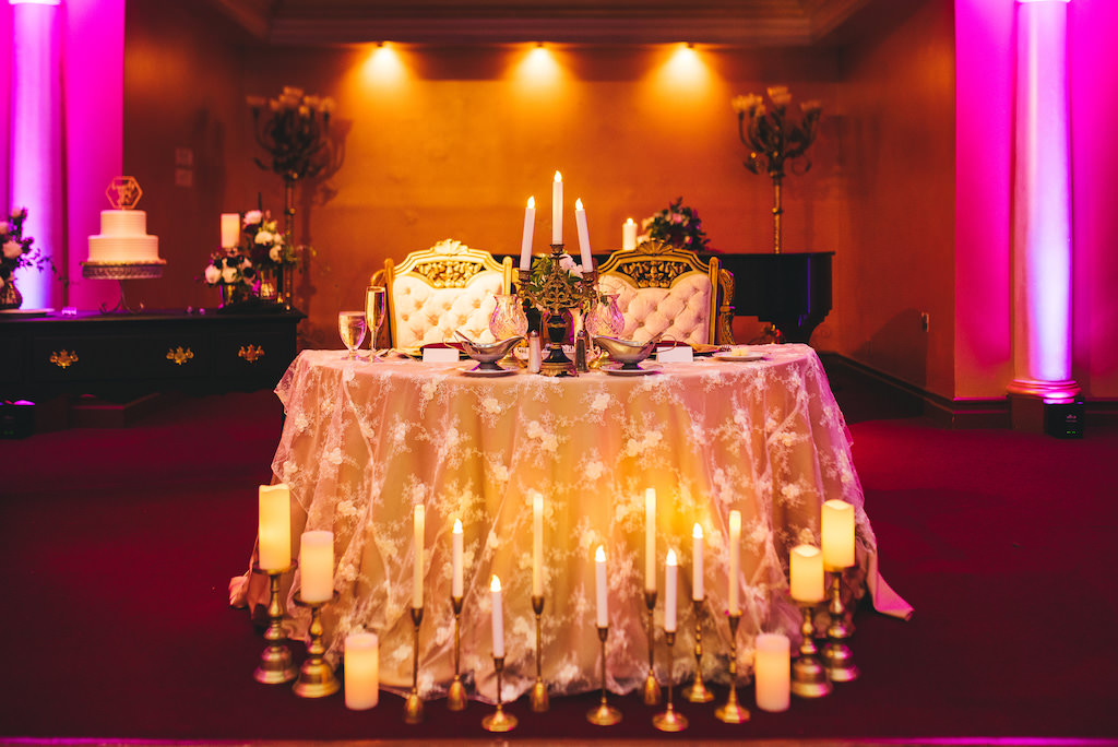 Modern Vintage Wedding Reception Decor, Sweetheart Table with Gold Tablecloth, Candlesticks and Vintage Chairs, Pink Uplighting | Venue Safety Harbor Resort and Spa