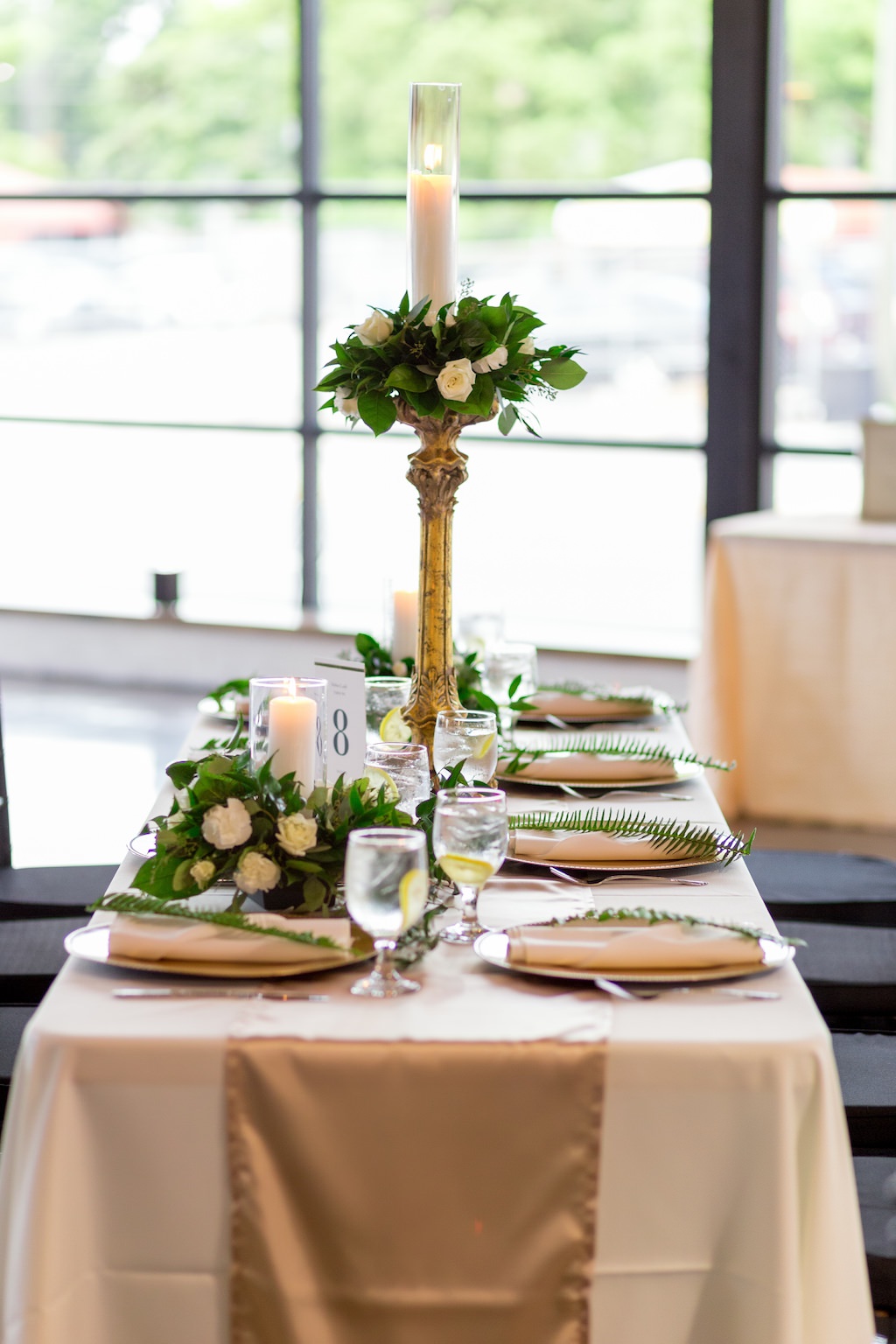 Wedding Reception Decor, Long Table with White Tablecloth, Gold Silk Table Runner, Gold Chargers, White Linen, Green Leaf, Tall Gold Candlestick with White Rose and Greenery Topper and Glass Cylinder Candle Holder | Tampa Bay Photographer Andi Diamond Photography | Rentals A Chair Affair