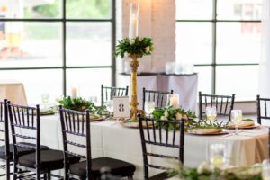 Wedding Reception Decor, Long Table with White Tablecloth, Gold Silk Table Runner, Gold Chargers, White Linen, Green Leaf, Tall Gold Candlestick with White Rose and Greenery Topper and Glass Cylinder Candle Holder and Black Chiavari Chairs | Tampa Bay Photographer Andi Diamond Photography | Rentals A Chair Affair