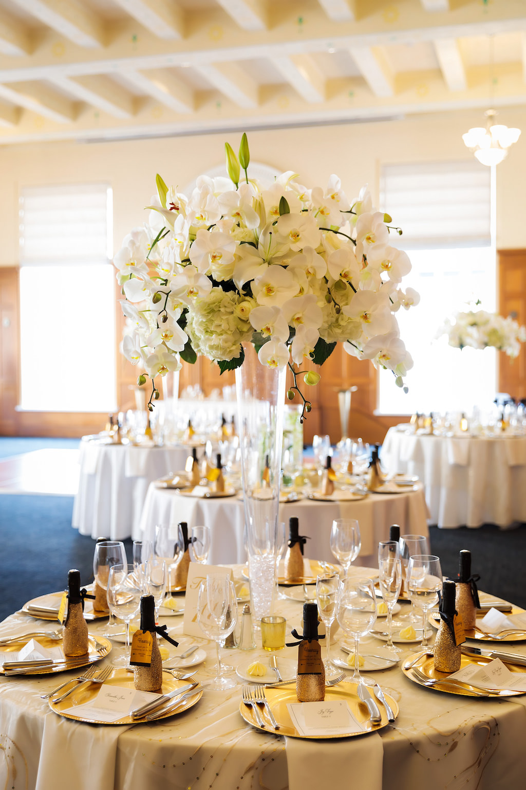Hotel Ballroom Wedding Reception with Round Tables, Tall Glass Vases with White Orchids Centerpieces, White Tablecloths and Mini Champagne Bottles | Historic Courthouse Downtown Tampa Hotel Venue Le Meridien | Rentals Kate Ryan Linens