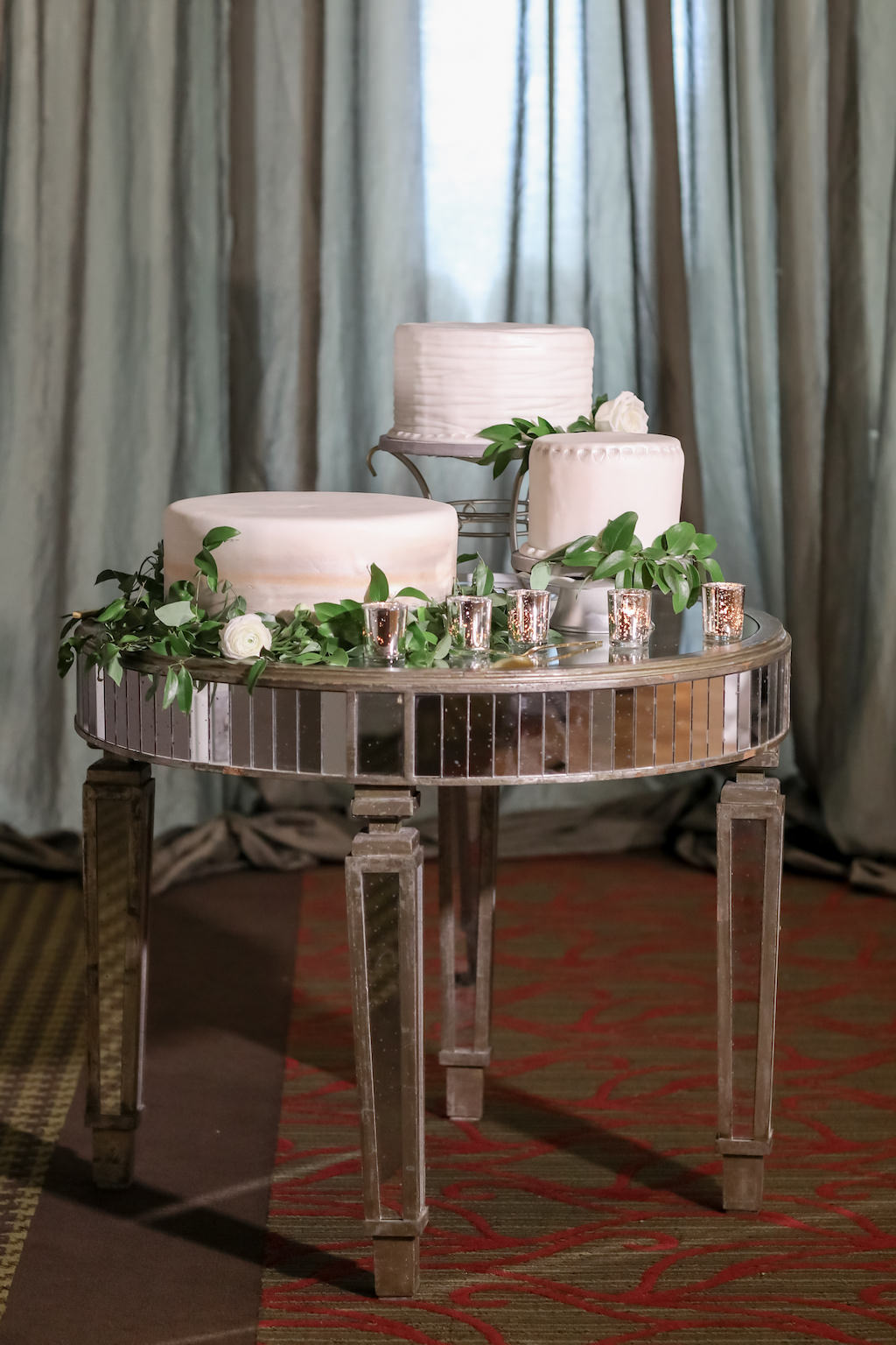 Deconstructed Three One Tier White Wedding Cakes on Various Cake Stands with Greenery and White Roses on Mirror Round Table and Silver Votives | Tampa Bay Photographer Lifelong Photography Studios | Planner Parties A'la Carte | Wedding Cake Alessi Bakeries | Rentals A Chair Affair | Florist Cotton and Magnolia