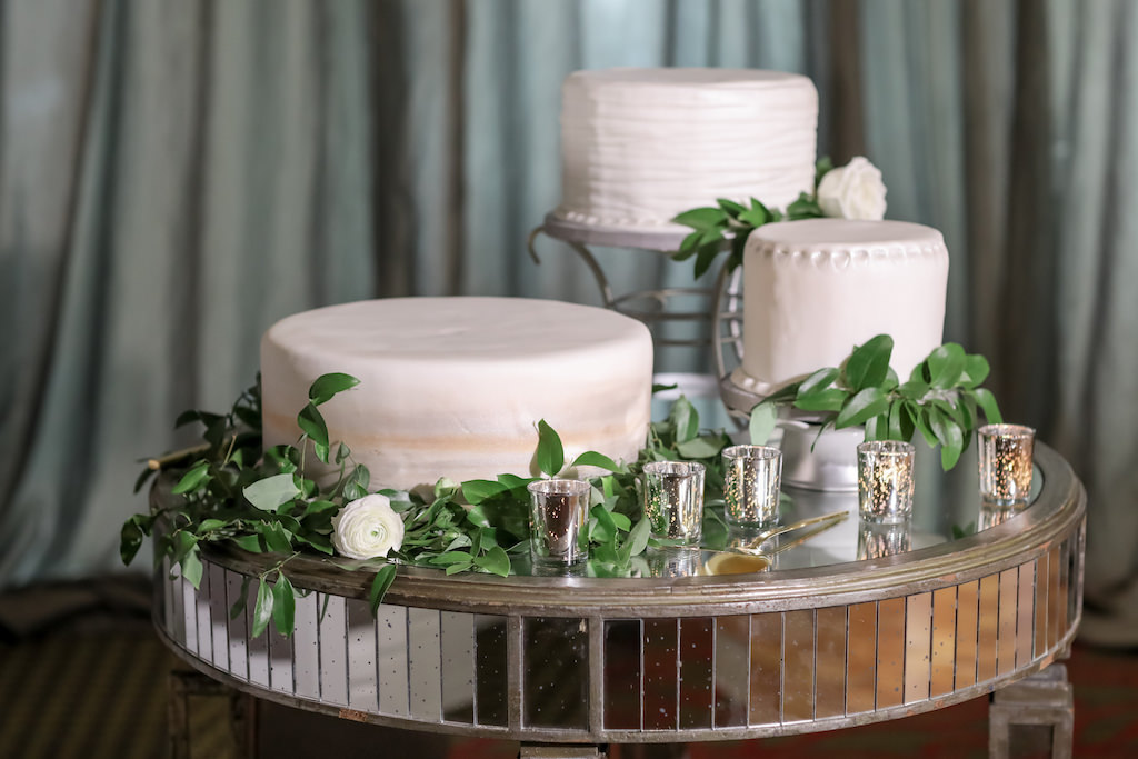 Deconstructed Three One Tier White Wedding Cakes on Various Cake Stands with Greenery and White Roses on Mirror Round Table and Silver Votives | Tampa Bay Photographer Lifelong Photography Studios | Planner Parties A'la Carte | Wedding Cake Alessi Bakeries | Rentals A Chair Affair | Florist Cotton and Magnolia