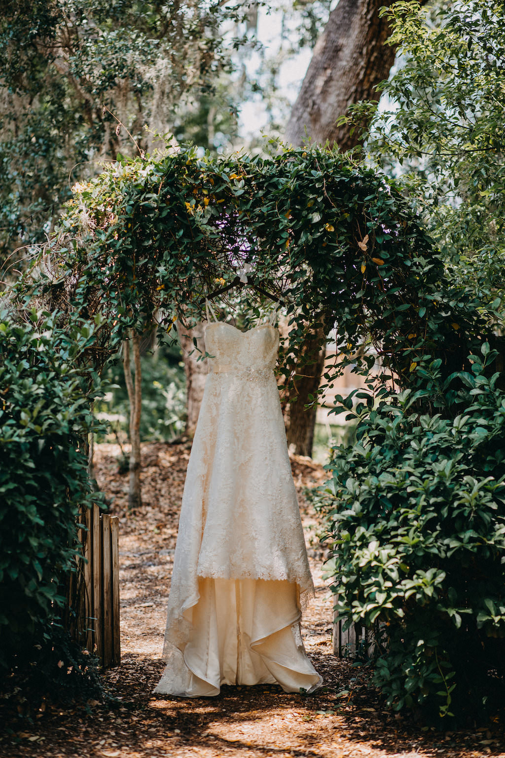 Strapless Sweetheart Neck Line Lace Wedding Dress Hanging Outside on Greenery Arch Doorway | Tampa Bay Photographer Rad Red Creative