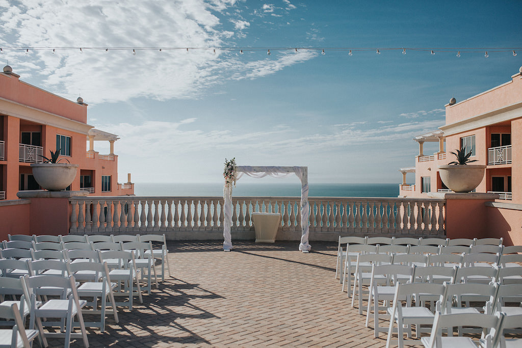 Waterfront Hotel Rooftop Wedding Ceremony with White Folding Chairs, Arch Wrapped with White Linen | Venue Hyatt Regency Clearwater Beach