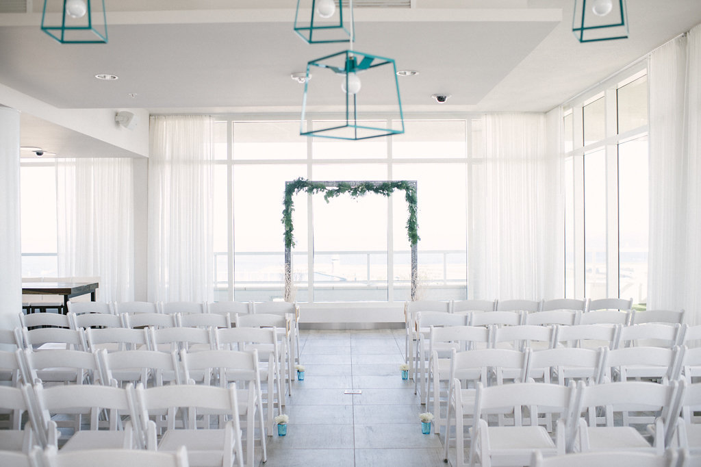 Wedding Ceremony Decor, Wooden Arch with Greenery Garland, White Folding Chairs, Blue Vases with White Flowers in Aisle | St. Petersburg Unique Venue Camden Pier District Apartments