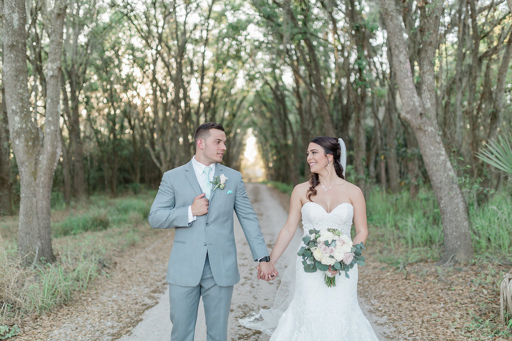 Outdoor Bride and Groom Tampa Bay Wedding Portrait, Bride in Strapless Sweetheart Lace Fit and Flare Wedding Dress with Blush Pink, Ivory and Greenery Floral Bouquet, Groom in Grey Suit with Mint Green Tie