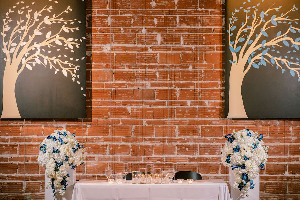 Wedding Reception Decor, Sweetheart Table, White Hydrangeas and Blue Orchids Floral Arrangements on White Pedestals | Industrial Brick Wall Downtown St. Pete Wedding Venue NOVA 535