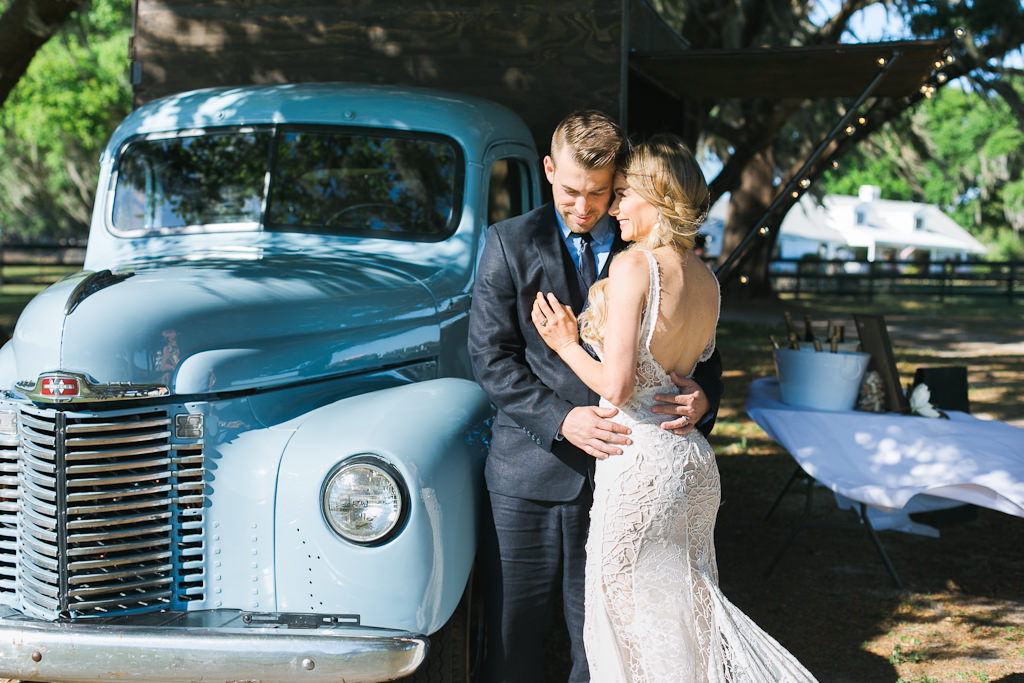 Outdoor Rustic Bride and Groom Wedding Portrait in Front of Vintage Baby Blue Truck, Bride in Sleek Low Back Lace Wedding Dress with Straps, Groom in Navy Blue Suit | Tampa Bay Wedding Venue Covington Farm Weddings | Tampa Wedding Dresses Isabel O'Neil Bridal