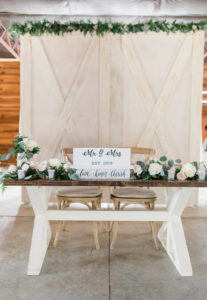 Rustic Elegant Barn Wedding Reception Decor, Wooden Sweetheart Table, Wood Chiavari Chairs, White Wood Mr and Mrs Sign, Blush Pink, Ivory Rose and Greenery Florals, White Wash Wooden Barn Door Backdrop with Greenery Garland