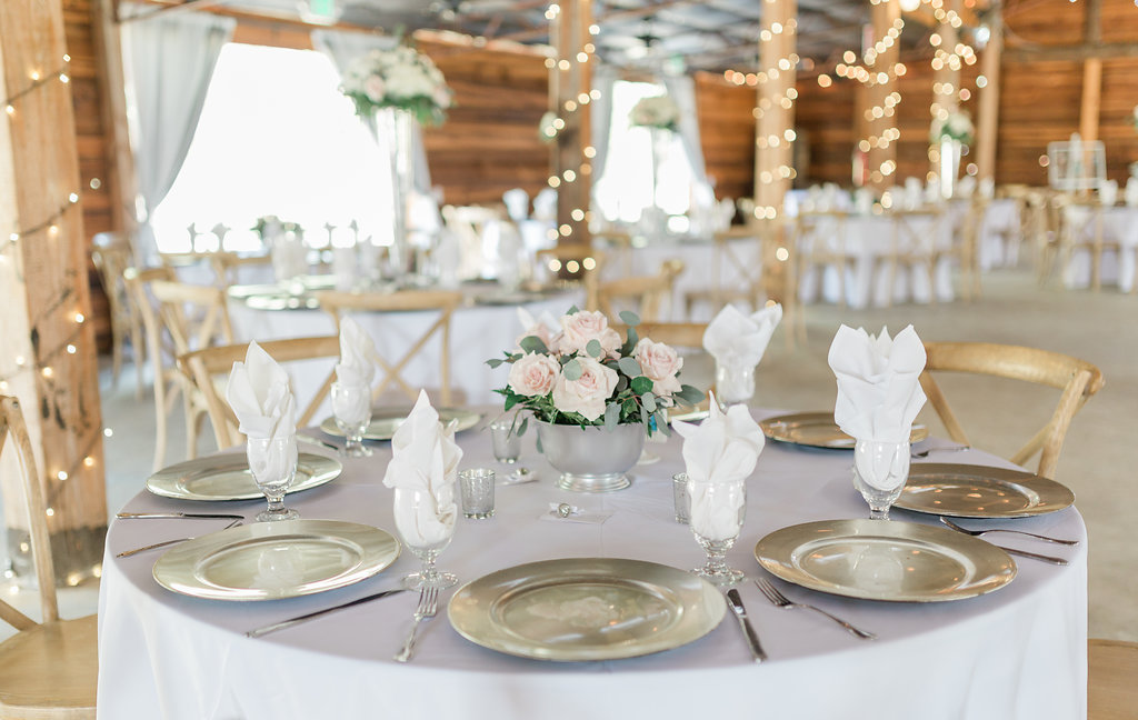 Rustic Elegant Tampa Bay Barn Reception Decor, Round Tables with Grey Tablecloths, Silver Chargers, Low Blush Pink and Green Leaf Floral Centerpiece in Silver Vase, Wood Chiavari Chairs | Plant City Wedding Venue Florida Rustic Barn Weddings