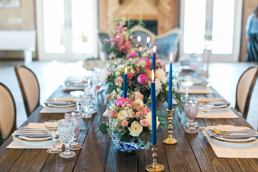 Vintage Elegant Wedding Reception Decor, Long Wooden Feasting Table, Blue Candlesticks, Pink, White and Greenery Floral Centerpieces in Blue and White Vases, Antique China on White Linens
