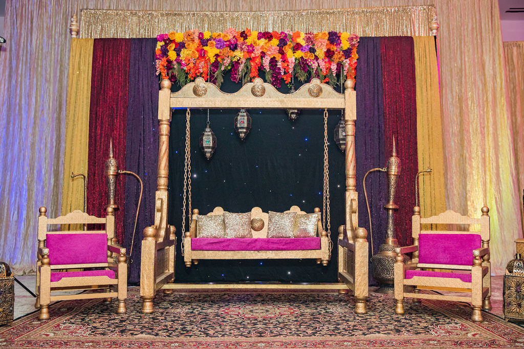 Glamorous Indian Wedding Reception Decor, Gold Swing with Purple and Gold Cushions with Colorful Pink, Purple, Orange, Yellow Flower Arch, Gold Chairs with Purple Cushions, Yellow, Dark Red, Purple and Gold Linen Backdrop | Tampa Bay Wedding Venue Wyndham Grand Clearwater Beach