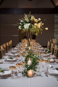 Modern, Elegant Wedding Reception Decor, Long Feasting Table with Tall Gold Stand with Organic Greenery and White Floral Centerpiece, Greenery Garland Table Runner, Candles and Gold Rimmer Glasses, Gold Chiavari Chairs | Tampa Bay Photographer Cat Pennenga Photography | Sarasota Wedding Planner NK Productions | Victoria Blooms