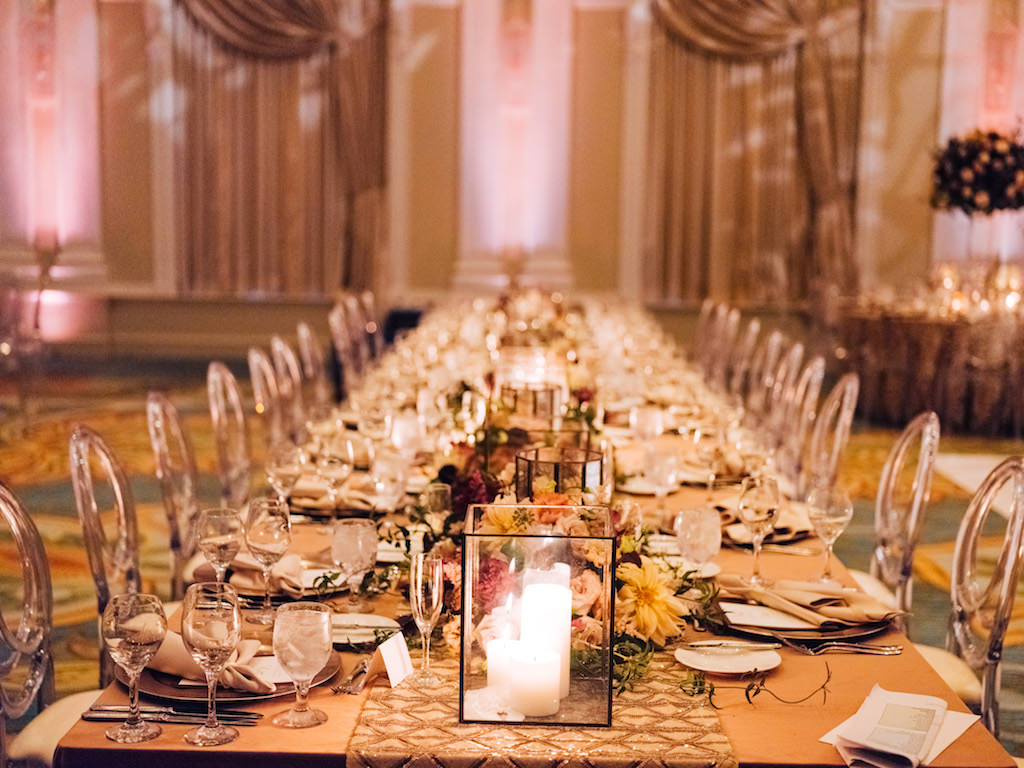 Elegant, Romantic Wedding Reception Decor, Long Feasting Table with Dark Gold Tablecloth, Gold Table Runner, Clear Glass Rectangular Glass Vases with Candles, Low Floral Centerpieces, Clear Acrylic Chairs with Ivory Cushions | Tampa Bay Wedding Planner Parties A'la Carte | St. Petersburg Wedding Hotel Venue The Vinoy Renaissance