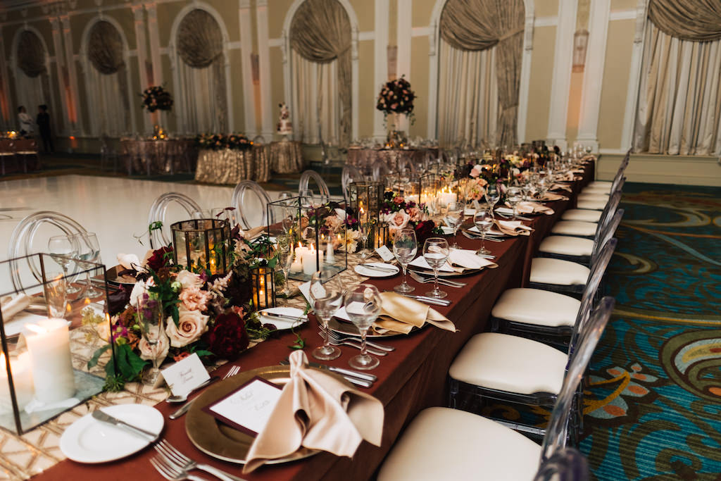 Elegant, Romantic Hotel Ballroom Wedding Reception Decor, Long Feasting Table with Burgundy Tablecloth, Gold Geometric Table Runner, Glass Rectangular Vase with Candles, Dusty Rose, Burgundy, Greenery Floral Bouquet Centerpieces, Clear Acrylic Chairs with Ivory Cushions | Tampa Bay Wedding Planner Parties A' la Carte | St. Petersburg Hotel Wedding Venue The Vinoy Renaissance