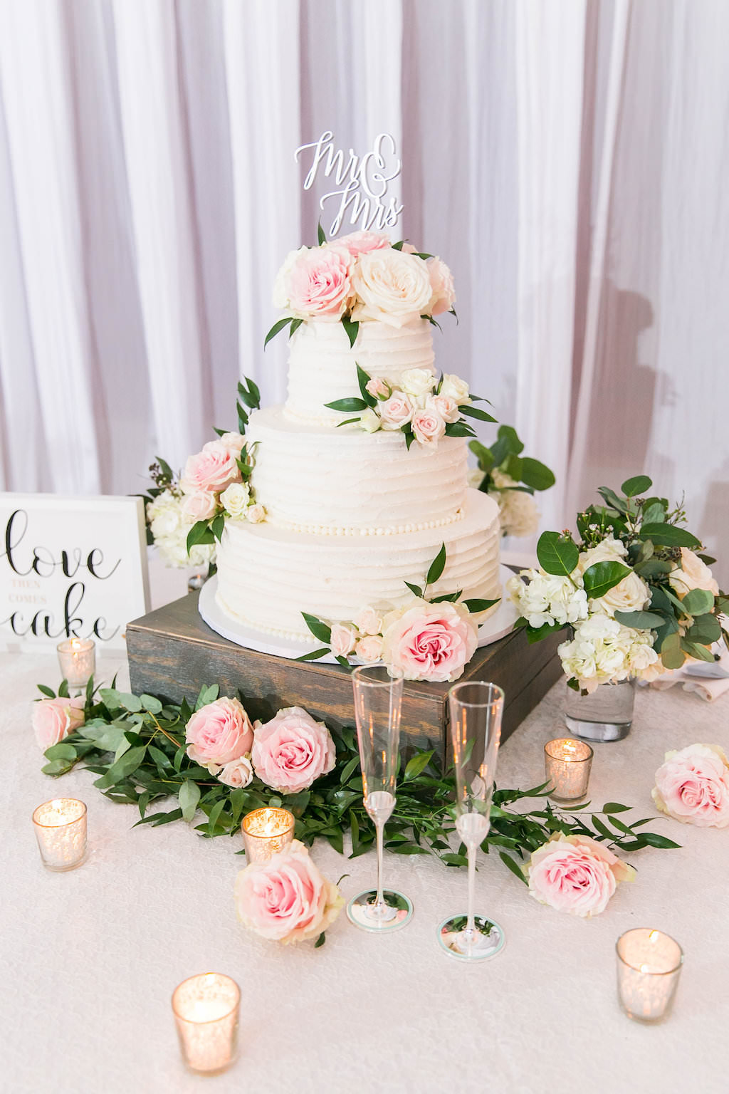 Three Tier Ruffle White Buttercream Cake with Real Blush Pink, Ivory and Greenery Florals on Wooden Cake Stand, Gold Votives and Custom Cake Topper