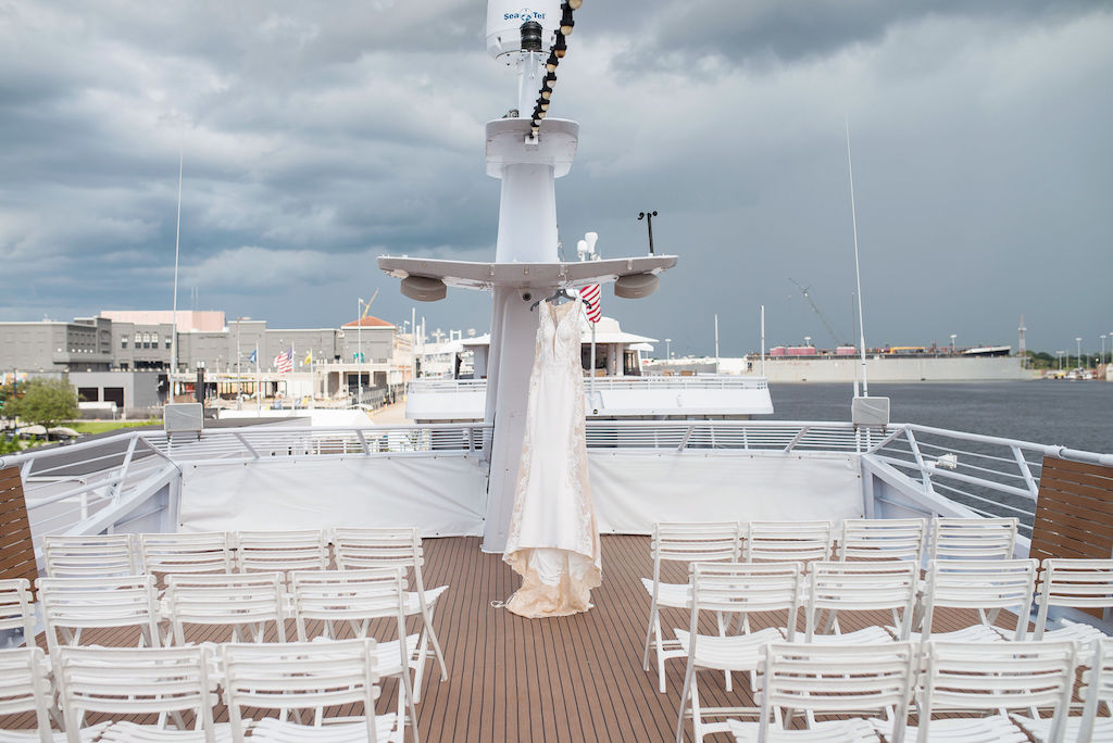 Deep V Neck Tank Top Strap Lace and Fitted Wedding Dress Hanging on Deck of Tampa Bay Waterfront Venue Yacht Starship II | Tampa Bay Wedding Photographer Kristen Marie Photography | Wedding Dress Nikki's Glitz and Glam Boutique