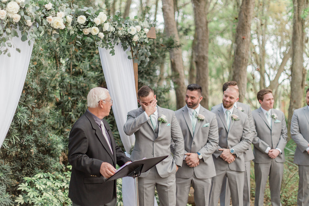 Outdoor Rustic Elegant Tampa Bay Wedding Ceremony Groom and Groomsmen Portrait in Grey Suits, Wooden Arch with White Linen Draping and Ivory Roses and Greenery Garland | Plant City Wedding Venue Florida Rustic Barn Weddings