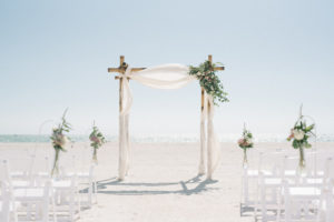 Outdoor Beach Wedding Ceremony Decor, Wooden Arch with White Linen Drapery, Greenery, White and Blush Pink Florals, White Wooden Folding Chairs, Floral Bouquets on Stands | Tampa Bay Photographer Kera Photography | St. Pete Beach Wedding Venue Tradewinds Island Resort