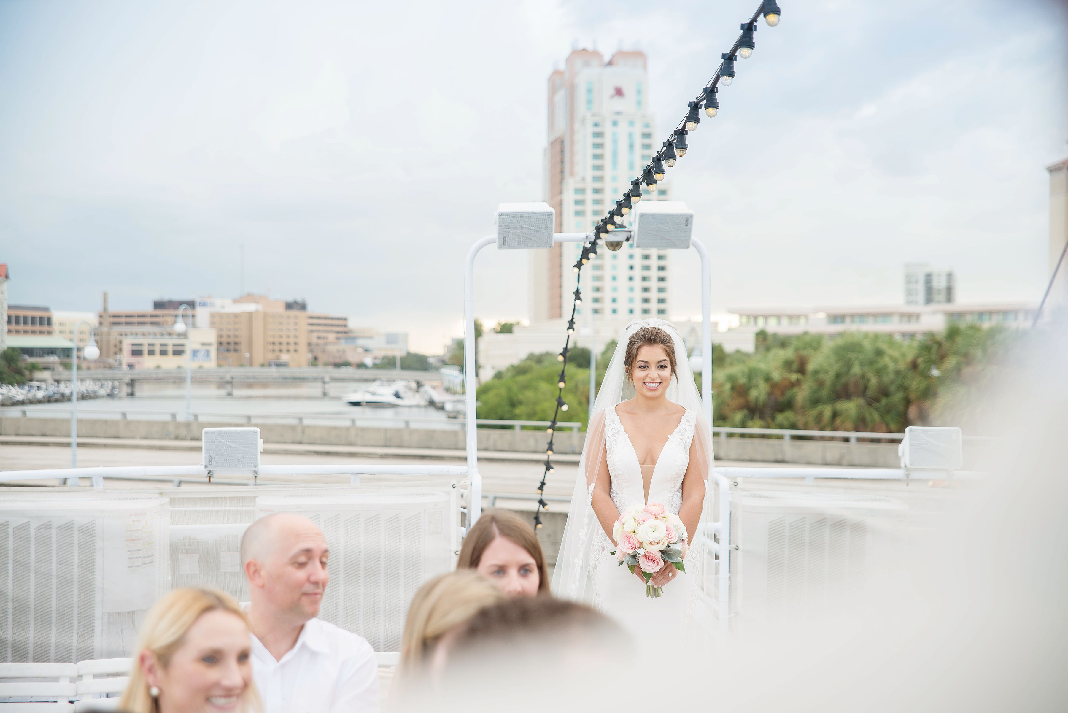 Florida Bride Wedding Ceremony Walking Down the Aisle Portrait in Deep V Neck Illusion Fitted Lace Tank Top Strap Wedding Dress with Blush Pink, Ivory and Dusty Miller Leaves Floral Bouquet | Tampa Bay Wedding Photographer Kristen Marie Photography | Wedding Dress Nikki's Glitz and Glam Boutique | Tampa Waterfront Venue Yacht Starship II | Hair and Makeup Destiny & Light Hair and Makeup Group