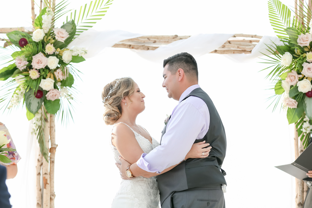 Clearwater Beach Waterfront Bride and Groom Wedding Ceremony Portrait Under Birchwood Arch with Blush pink, White and Red Florals with Green Palm Leaves | Tampa Bay Wedding Photographer Lifelong Photography Studios
