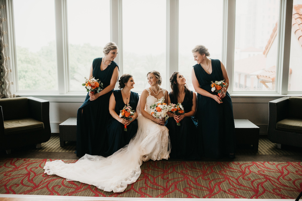 Florida Bride and Bridesmaid Wedding Portrait, Bride in Lace V-Neckline and Lace Strap Essense of Australia Wedding Dress, Bridesmaids in Matching Navy Blue Dresses with White and Orange Floral Bouquets