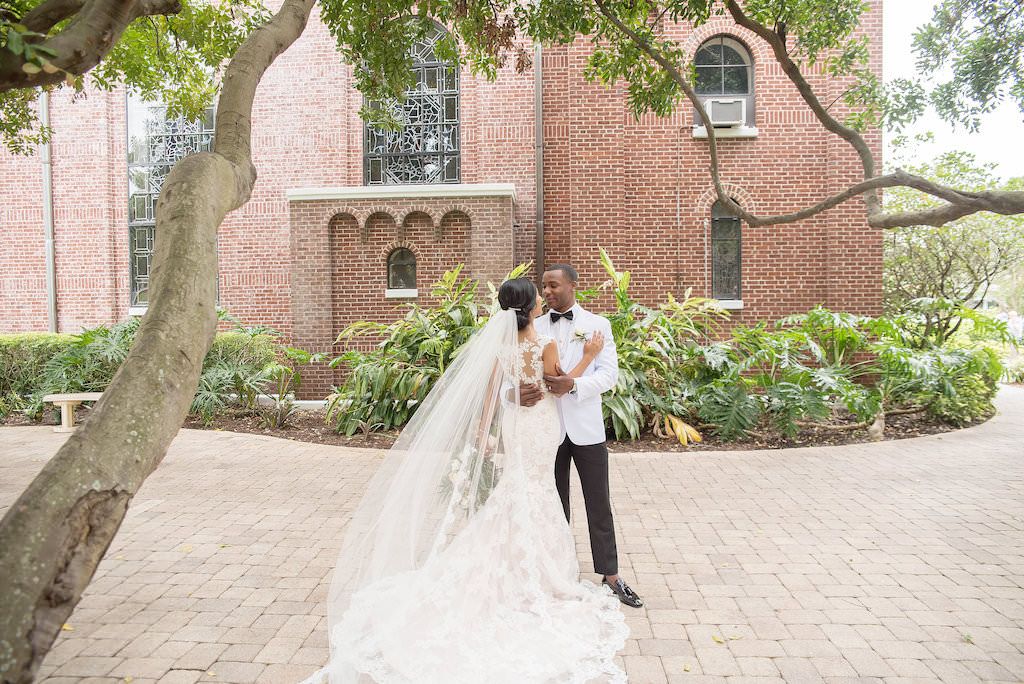 Florida Bride and Groom Outdoor Wedding Portrait, Bride in Fitted Lace and Illusion Cap Sleeve Allure Wedding Dress with Cathedral Length Veil, Groom in White Tuxedo | Tampa Bay Wedding Photographer Kristen Marie Photography | St. Pete Wedding Venue St. Paul's Catholic Church