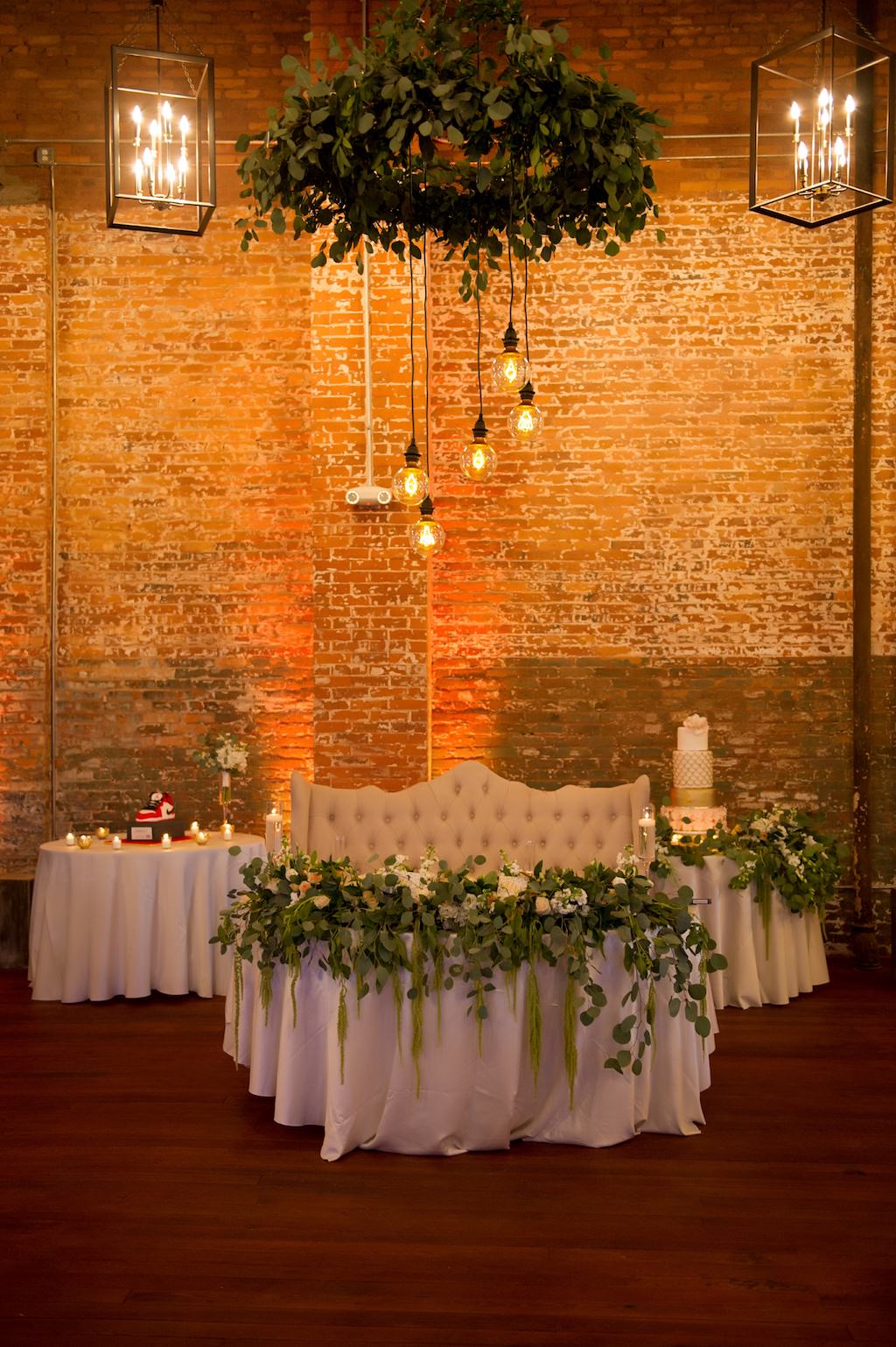 Industrial Chic Wedding Reception Decor, Sweetheart Table with White Tablecloth, Greenery and White Floral Garland, Off White Loveseat Lounge Seat, Greenery Chandelier | Tampa Bay Wedding Photographer Andi Diamond Photography | Unique Industrial Tampa Wedding Venue Armature Works