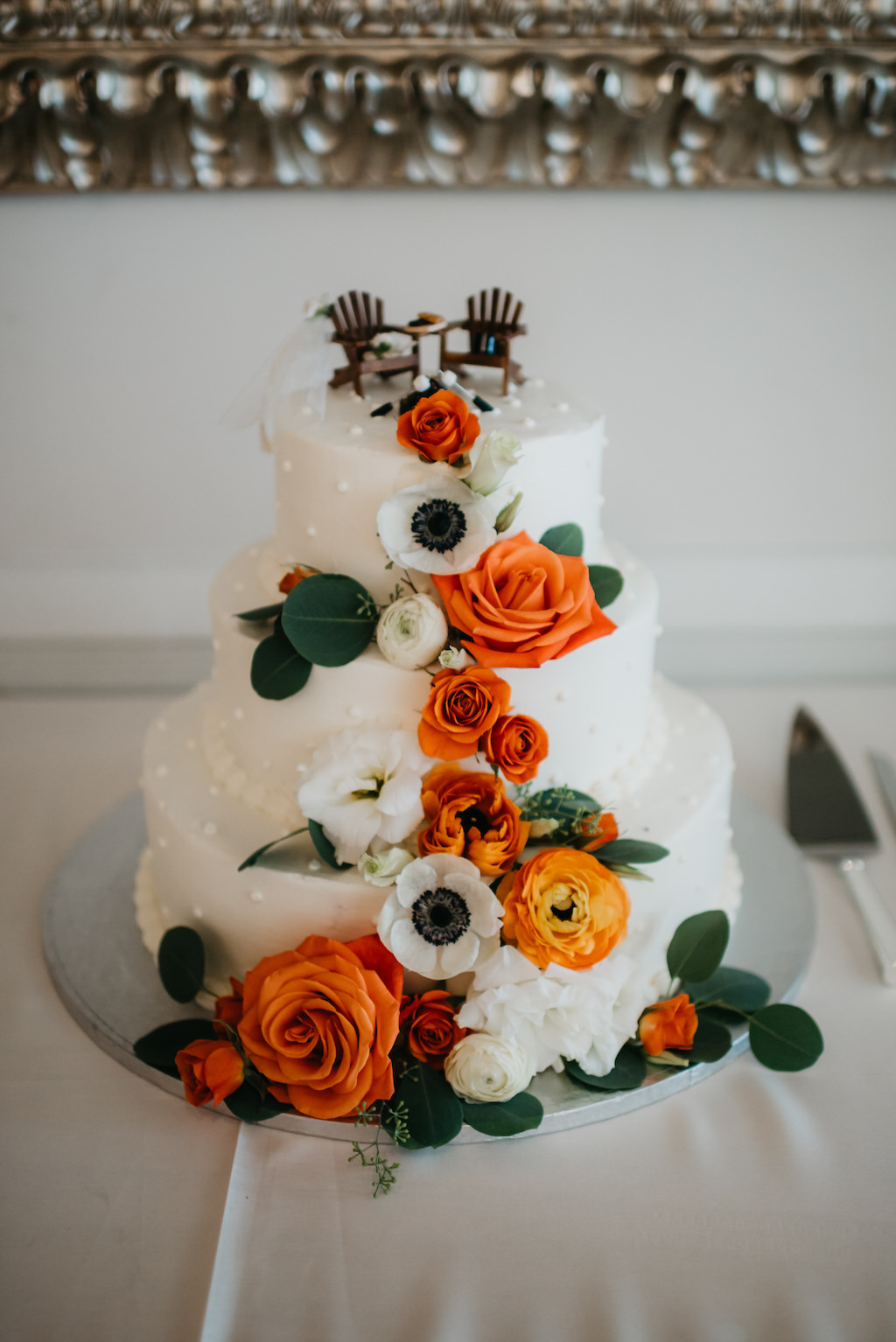 Three Tier White Wedding Cake with Orange, White Anemone and Greenery Cascading Real Florals with Adirondack Beach Chair Cake Toppers