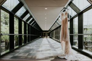 Illusion and Lace Off White Long Sleeve High Scoop Neckline Wedding Dress Hanging in Glass Window Hotel Tunnel Hallway | Tampa Bay Wedding Photographer Brandi Image Photography | Downtown Tampa Hotel Wedding Venue Hilton Tampa Downtown