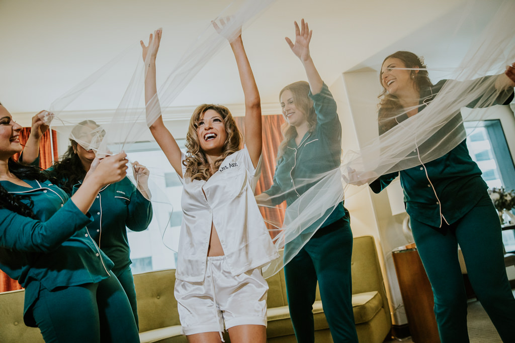 Bride and Bridesmaids Getting Ready Wedding Portrait Under Veil, Bridesmaids in Matching Green Long Sleeve Pajamas, Bride in Short Sleeve and Shorts White Pajamas | Tampa Bay Wedding Photographer Brandi Image Photography | Downtown Tampa Hotel Wedding Venue Tampa Hilton Downtown