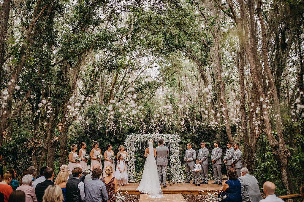 Elegant Outdoor Rustic Wedding Ceremony Decor, Bride and Groom Wedding Portrait, White and Greenery Floral Arch with Hanging Glass Bulbs | Lakeland Rustic Wedding Venue The Prairie Glenn Barn at Gable Oaks Ranch