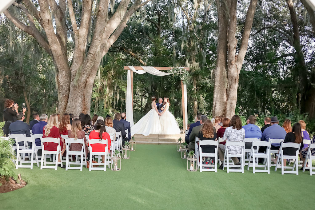 Outdoor Bride and Bride Wedding Ceremony Lesbian Gay Couple Portrait Under Wooden Arch with White Draping and Greenery and White Ivory Floral Bouquet | Tampa Bay Wedding Photographer Lifelong Photography Studio | Wedding Planner Love Lee Lane | Wedding Venue The Secret Garden at Paradise Spring