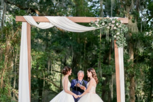 Outdoor LGBTQ Gay Same-Sex Bride Wedding Ceremony Lesbian Gay Couple Portrait Under Wooden Arch with White Draping and Greenery and White Ivory Floral Bouquet | Tampa Bay Wedding Photographer Lifelong Photography Studio | Wedding Planner Love Lee Lane | Wedding Venue The Secret Garden at Paradise Spring