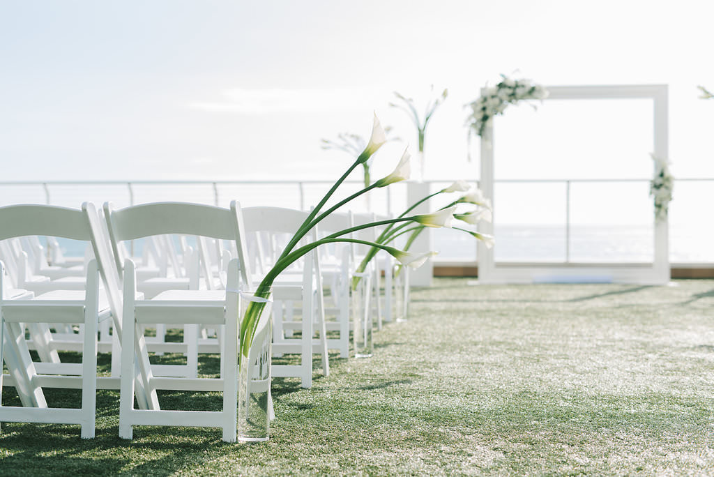 Modern Elegant Waterfront and Lawn Wedding Ceremony Decor, White Frame with Greenery and White Floral Arrangements, Tall White Pedestals with White Tulips, White Wooden Folding Chairs | Tampa Bay Wedding Photographer Kera Photography | Clearwater Beach Wedding Venue Opal Sands Resort